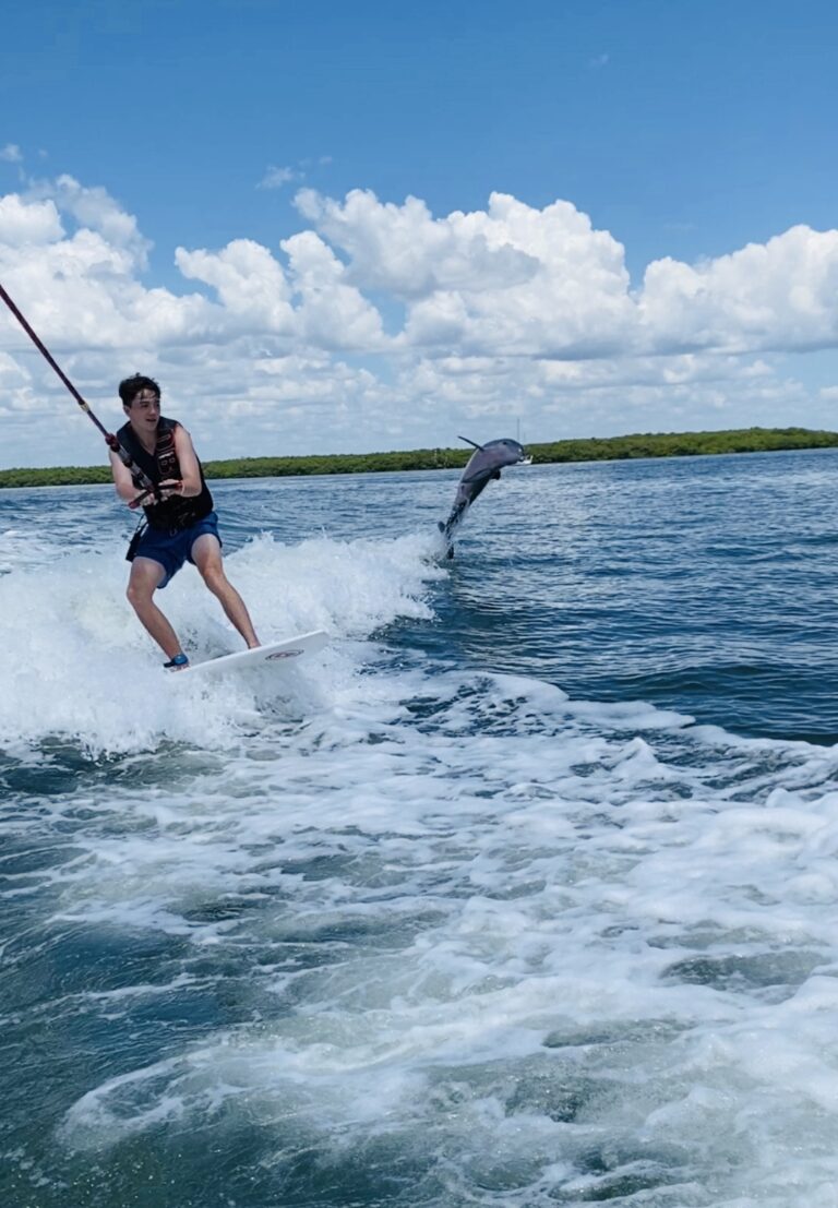 Male wakesurfing with dolphin jumping out of the water