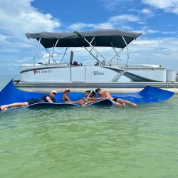 Family laying on float mat in front of white Pontoon boat